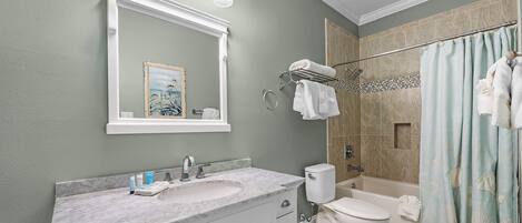 Un baño con lavamanos de mármol, inodoro, ducha con cortina y espejo con luces.