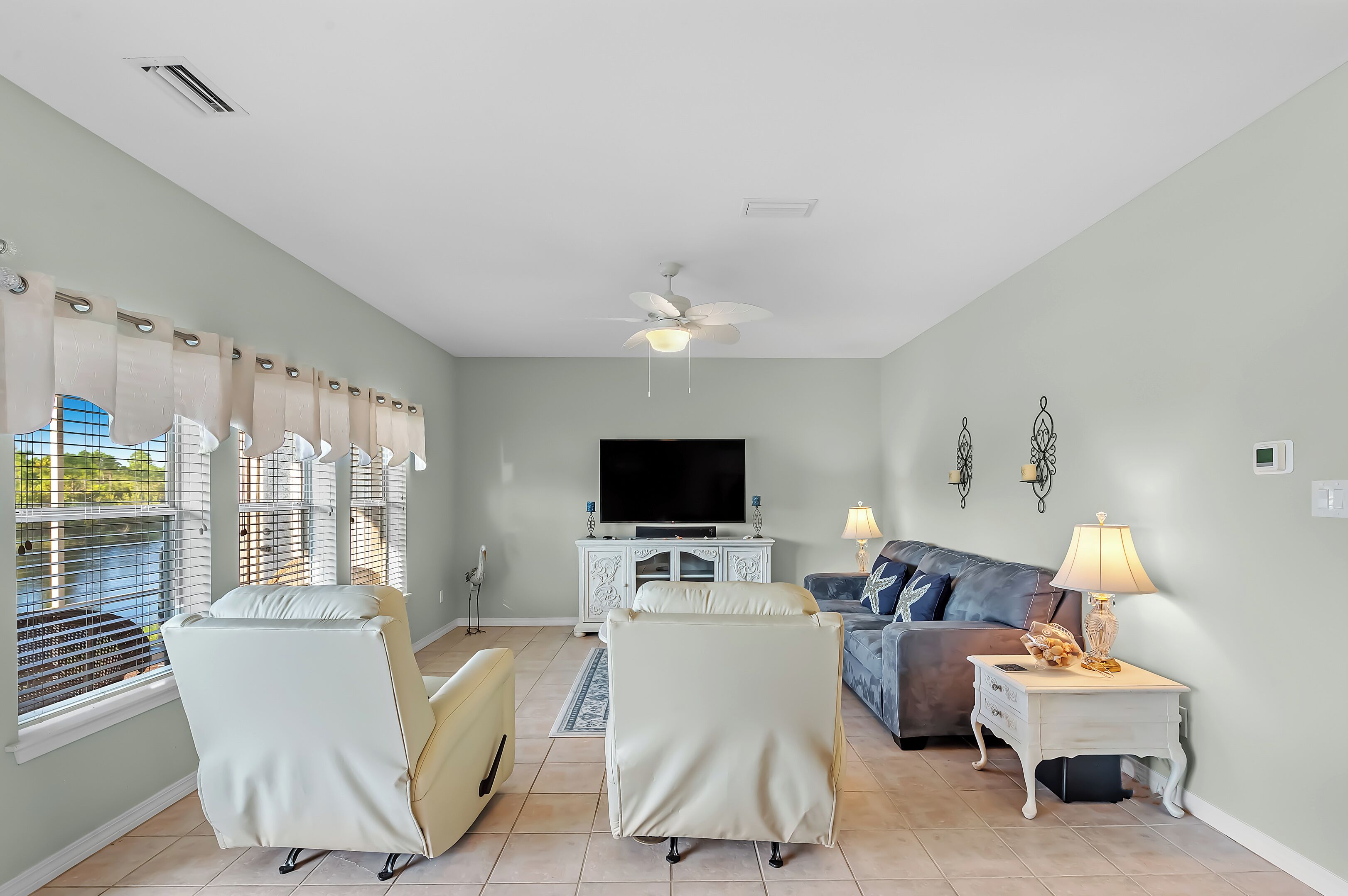A living room with a flat-screen TV, a ceiling fan, and a sofa.