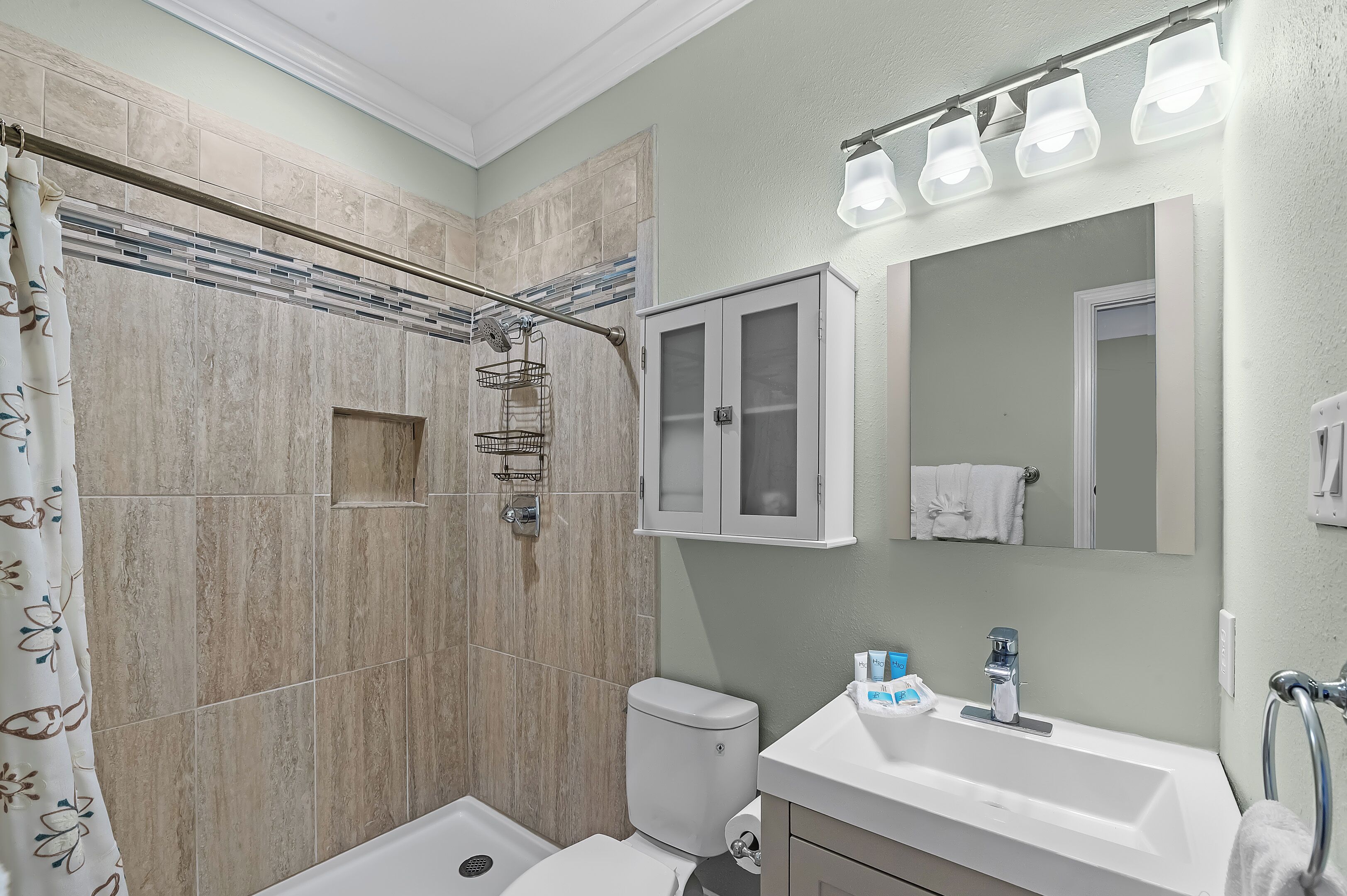 A bathroom with a shower, toilet, sink, and a cabinet with a mirror.