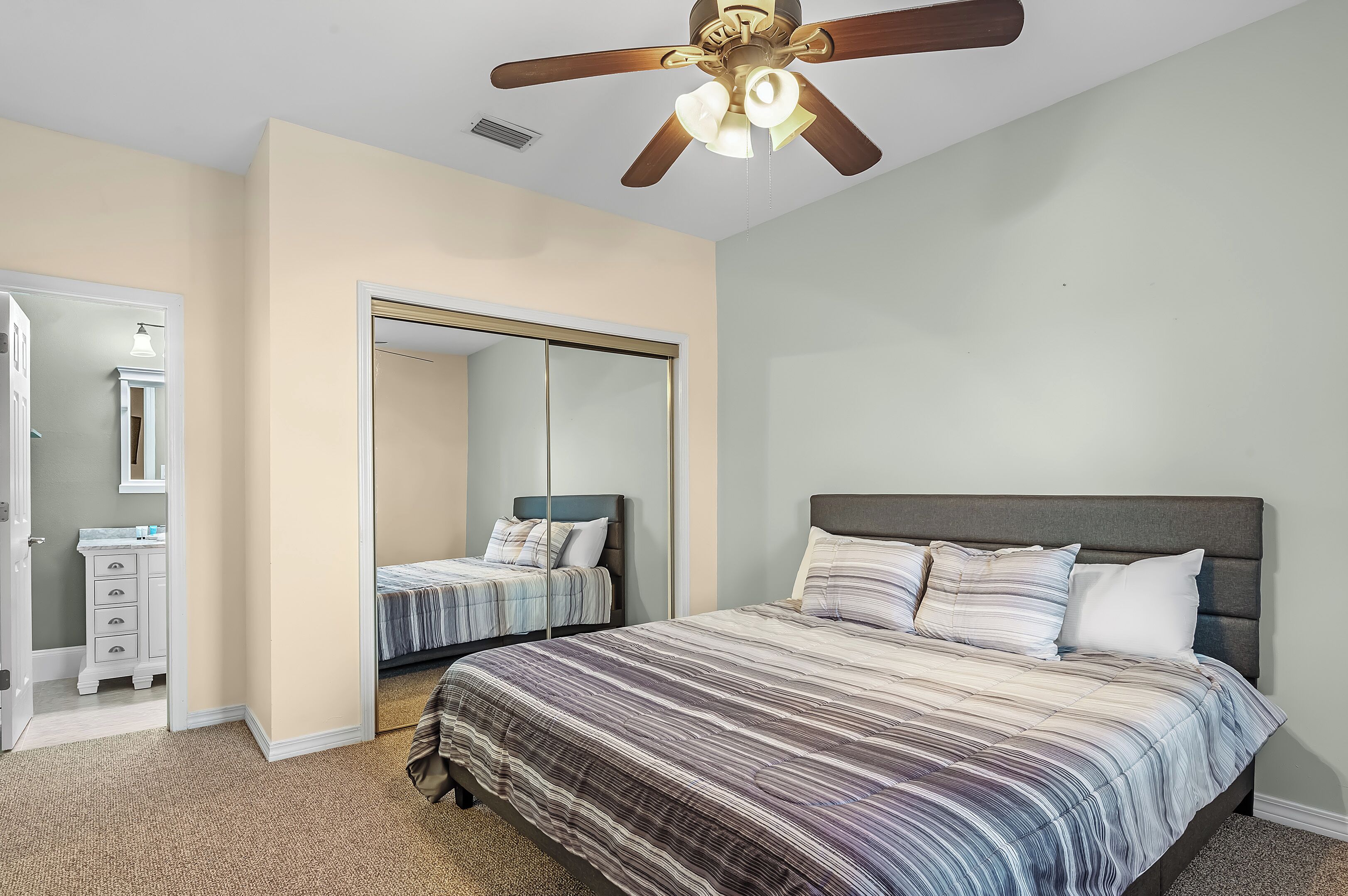 A bedroom with a large bed, a ceiling fan, a mirror, and a walk-in closet.
