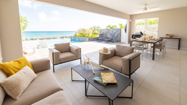 A spacious living area with a view of the ocean, a dining table set with food, and a cozy seating arrangement. - Villa Koh-I-noor (Le Diamant)