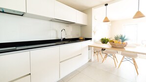 A modern kitchen with white cabinets, a black countertop, and a dining area with a wooden table and chairs. - Villa Koh-I-noor (Le Diamant)