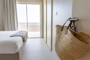 Hotelkamer met een bed, een geweven mand en uitzicht op het strand door een schuifdeur.
