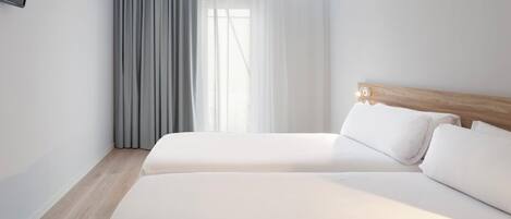 Una habitación de hotel con cama doble, cabecero de madera y un ventanal con cortinas traslúcidas.