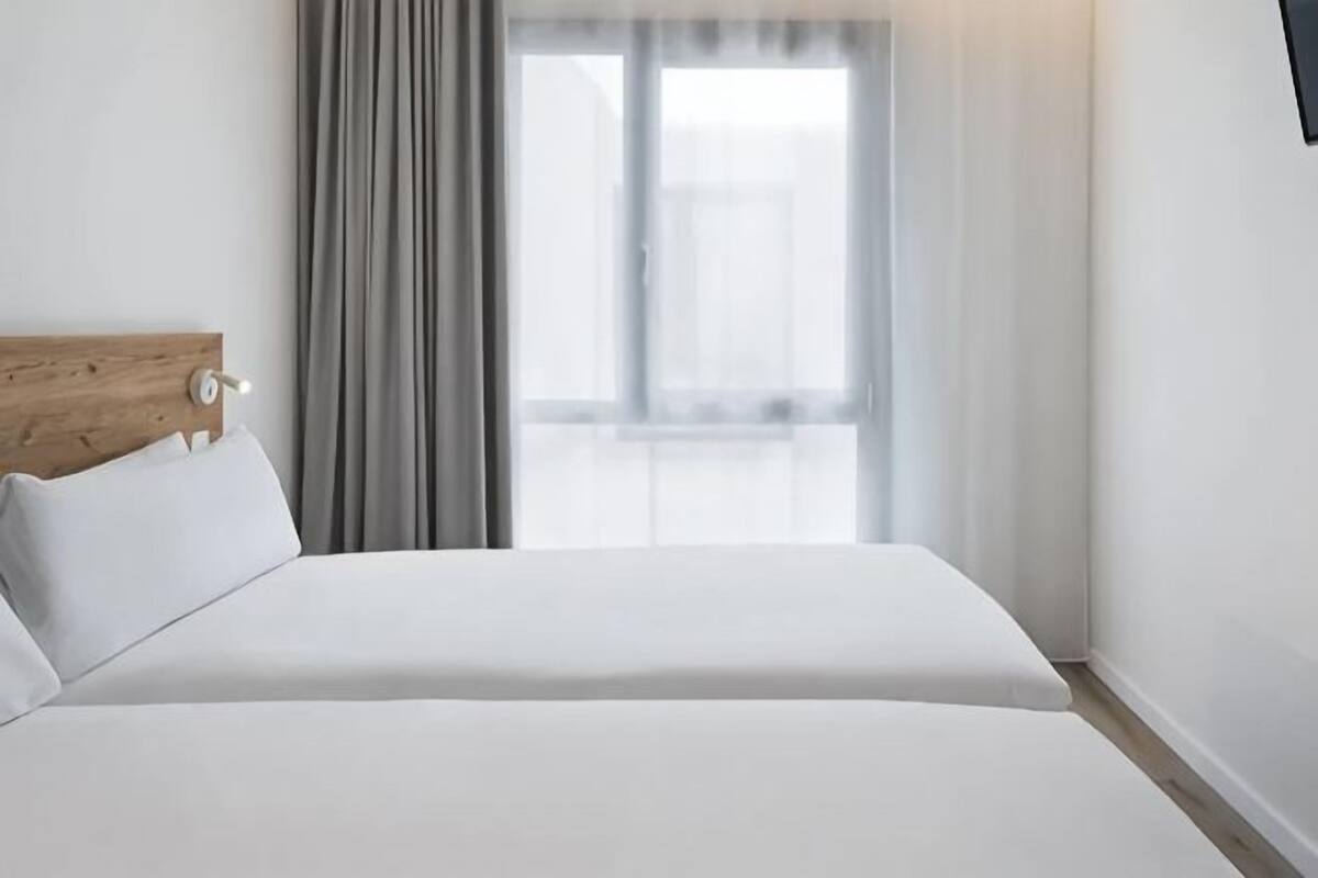 Habitación de hotel con cabecera de madera, cama grande, ventana con cortinas y vistas al exterior.