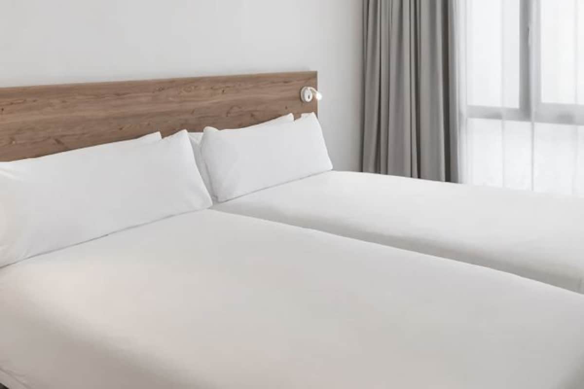 Una cama doble con cabecera de madera, ropa de cama blanca y una ventana con cortinas.
