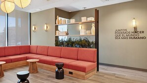 Ein stilvoller Lounge-Bereich mit einem roten Ecksofa, Holztischen und einer Wand mit Regalen, auf denen dekorative Gegenstände präsentiert werden.