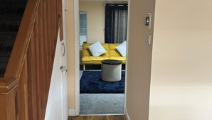 A hallway leading to a bedroom with a bed, a nightstand, and a window with curtains. - Cozy Basildon Retreat With 3 Bedrooms Free Parking (Basildon)