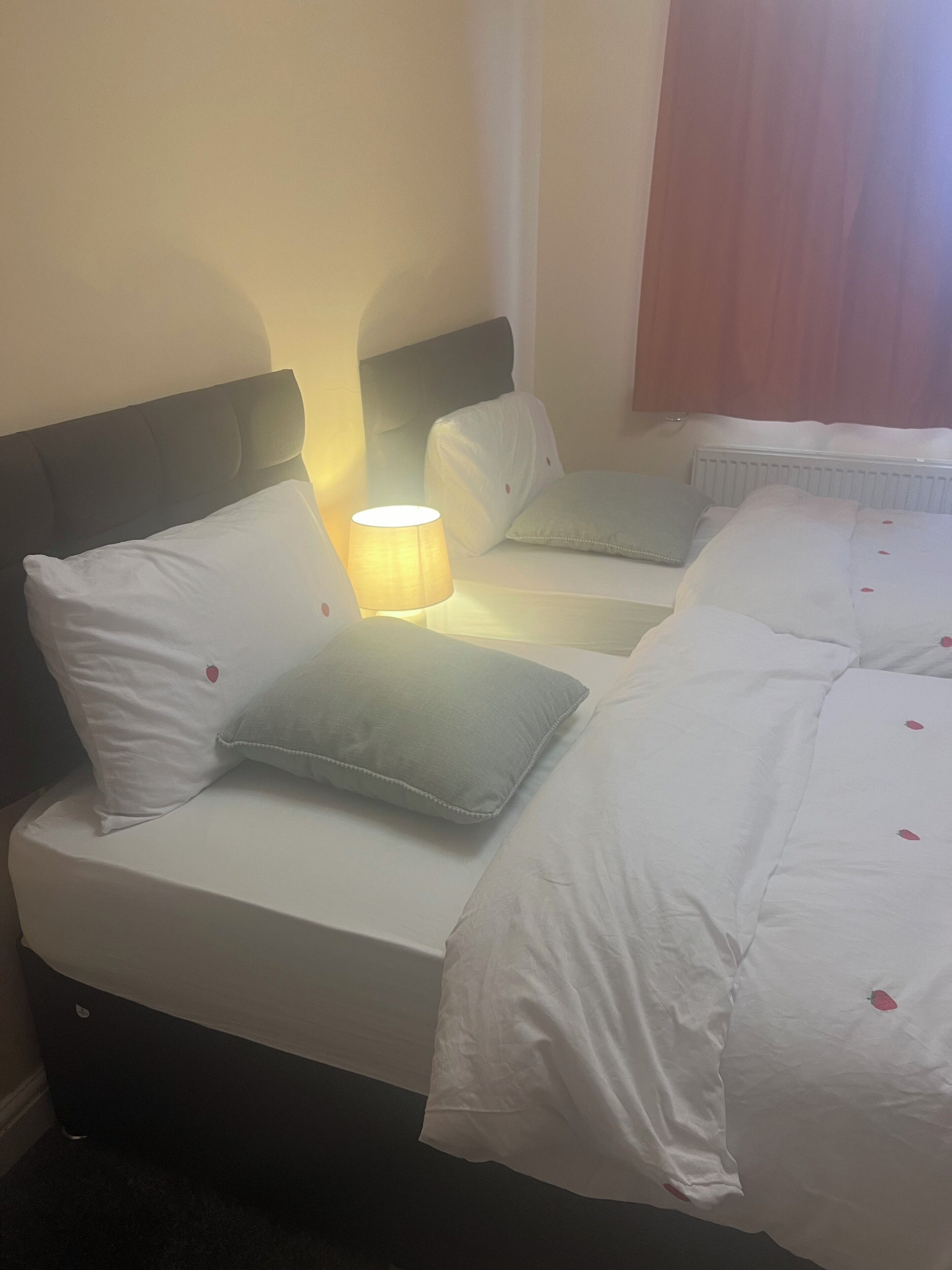 A hotel room with a bed, pillows, a bedside lamp, and a window with curtains.