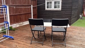A wooden deck with two black chairs and a table, a wooden fence, and a small shed with a window. - Cozy Basildon Retreat With 3 Bedrooms Free Parking (Basildon)