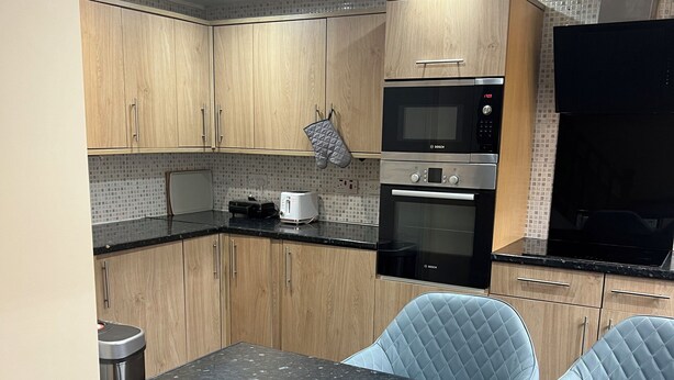 A modern kitchen with wooden cabinets, a black countertop, a Bosch microwave, and a toaster. - Cozy Basildon Retreat With 3 Bedrooms Free Parking (Basildon)