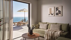 A modern living room with a sofa, a coffee table, and a view of the ocean through a large window.