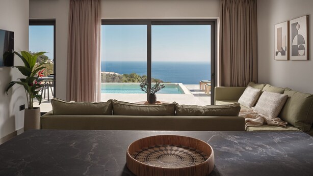 A modern living room with a large window, a sofa, a coffee table, and a view of the sea.