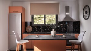 A modern kitchen with a central island, two white bar stools, a refrigerator, a stove, and a window with a view of greenery.
