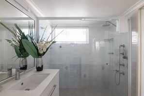 A modern bathroom with a glass-enclosed shower, a large mirror, and a vase with white flowers.