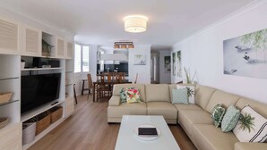 Ein modernes Wohnzimmer mit Sofa, Couchtisch, Fernseher und einem Essbereich mit Stühlen und Tisch.