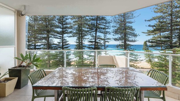 Ein Balkon mit Glastisch und Stühlen, mit Blick auf Strand und Wald.