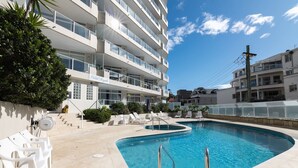 Ein Pool mit geschwungener Kante, umgeben von weißen Liegestühlen und einer Treppe, die zu einem Balkon führt.