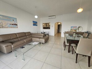 A modern living room with a sectional sofa, a glass coffee table, and a dining area with a glass table and chairs.