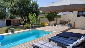 Une terrasse en bois avec une piscine, des chaises longues et un espace patio couvert.