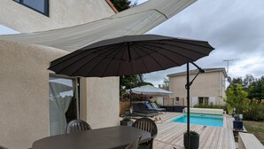 Une terrasse avec une table et des chaises, une piscine et des parasols.