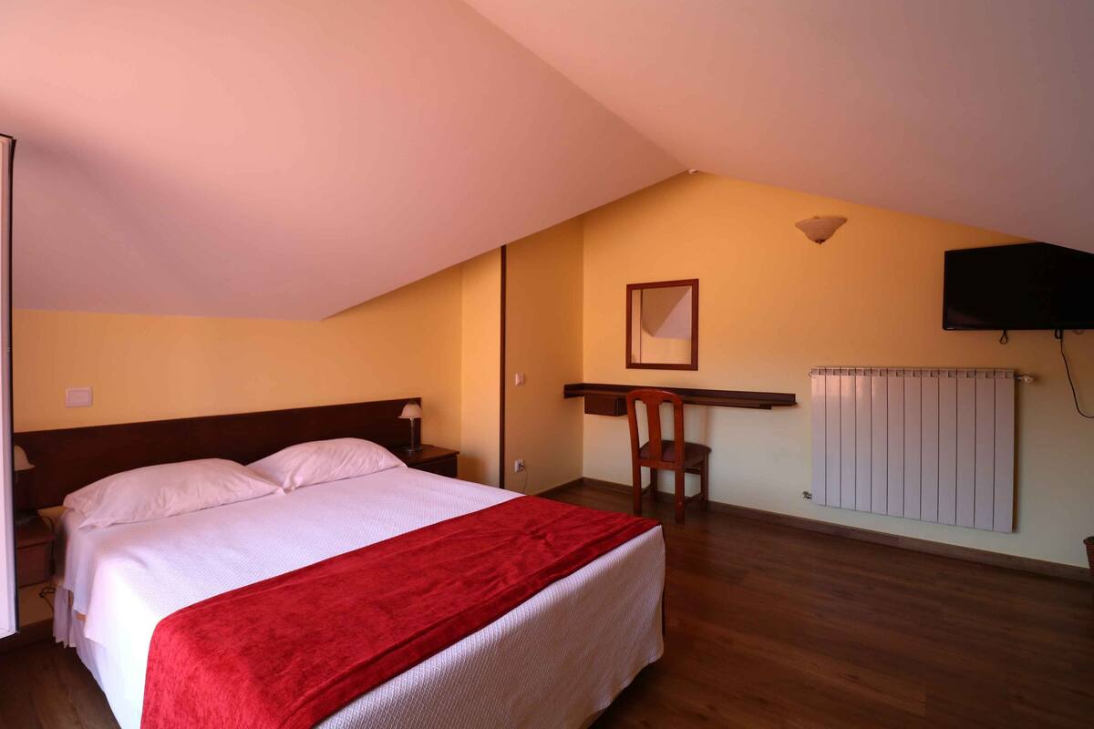 A bedroom with a bed, a desk, a chair, and a TV.