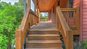 Un escalier en bois mène à un porche doté d’une balustrade, le tout entouré de verdure.