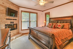 A bedroom with a large bed, a TV mounted on the wall, and a ceiling fan.