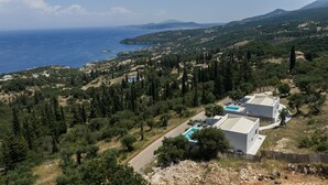 En ejendom ved kysten med swimmingpool, omgivet af frodig vegetation og havudsigt.