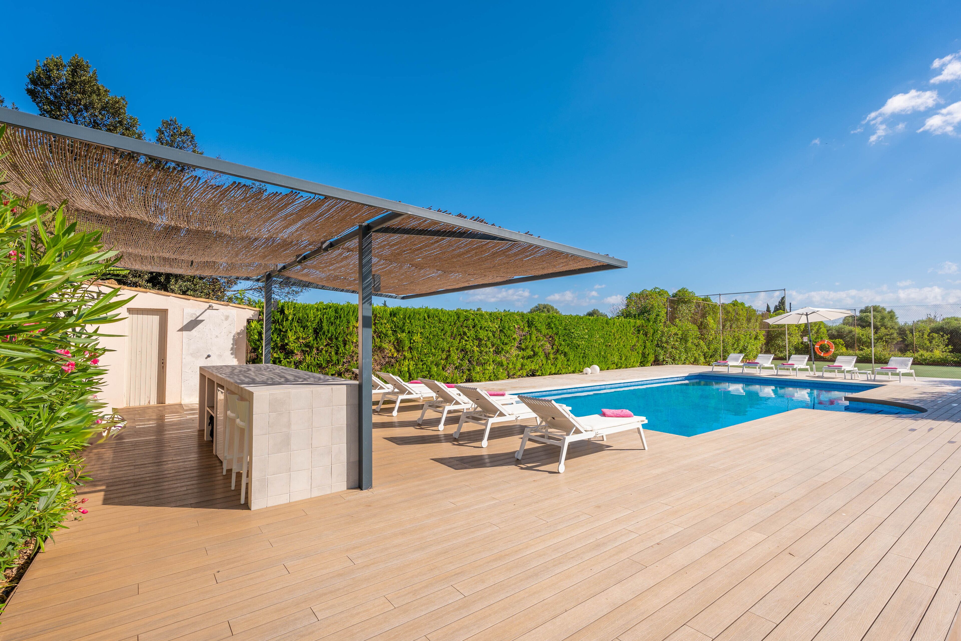 A poolside area with a wooden deck, white lounge chairs, and a covered seating area.
