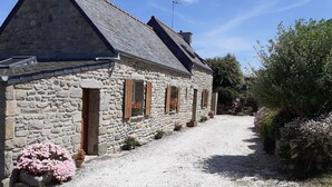 Un bâtiment en pierre avec un toit en pente, des volets en bois et une allée gravillonnée.