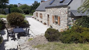 Un bâtiment en pierre avec une allée de gravier, une table et des chaises, et des plantes en pot.
