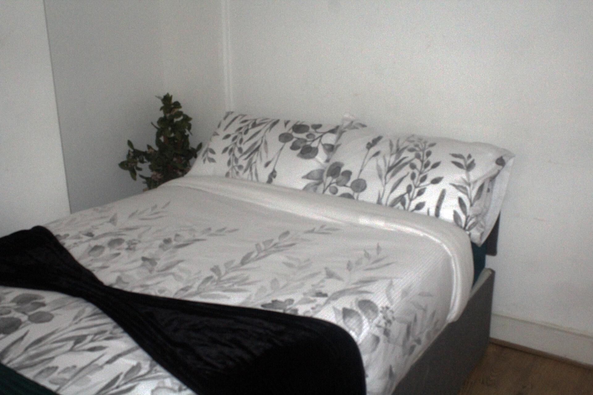 A bed with a floral-patterned bedspread and pillows, a dark-colored blanket, and a small potted plant beside the bed.