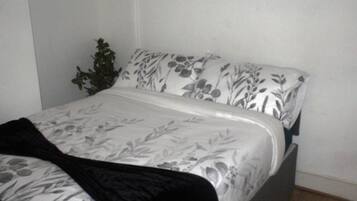 A bed with a floral-patterned bedspread and pillows, a dark-colored blanket, and a small potted plant beside the bed.