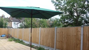 Una zona patio con un ombrellone verde, recinzione in legno e pavimento piastrellato.