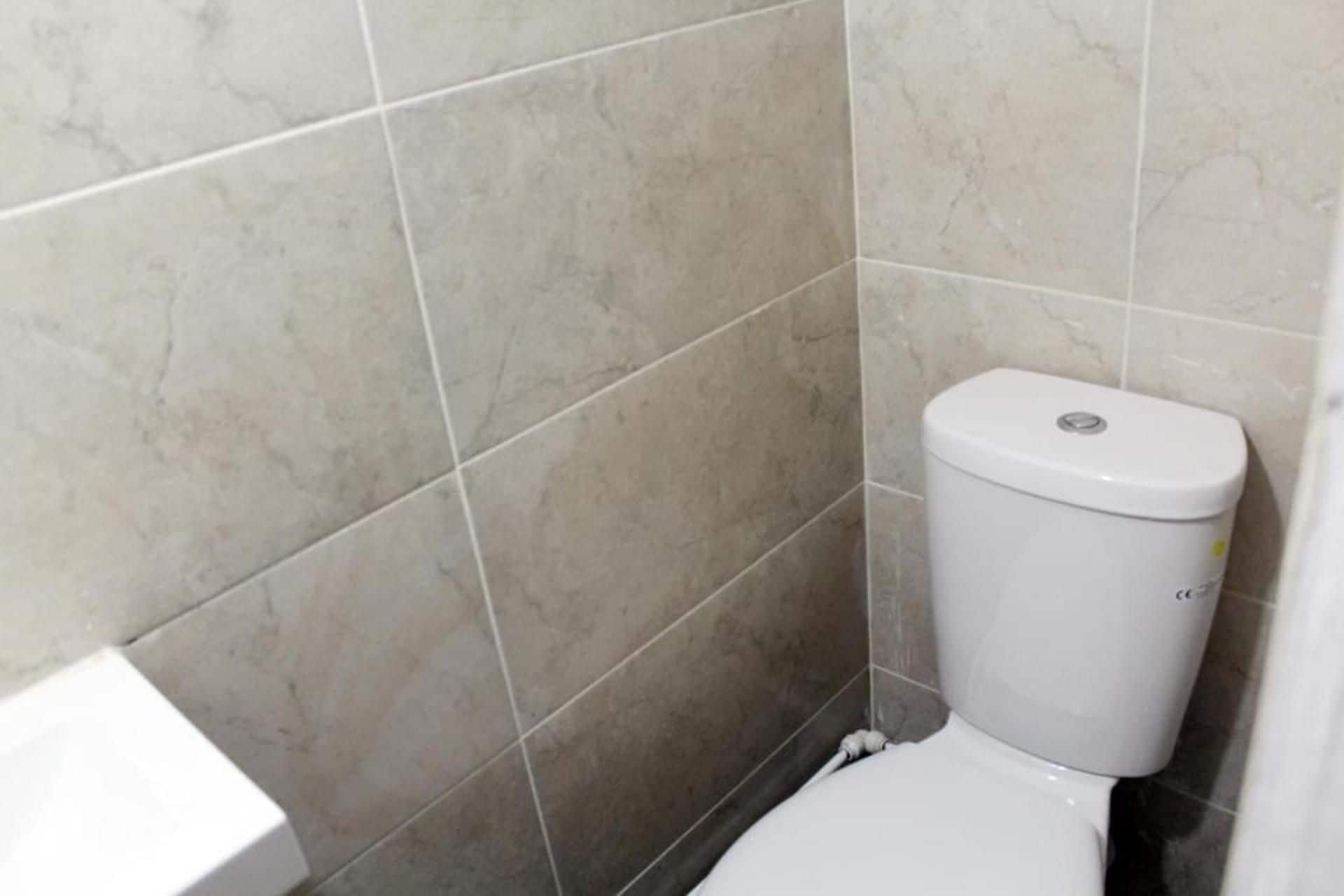 Une salle de bain avec des toilettes, des murs carrelés et un lavabo blanc.