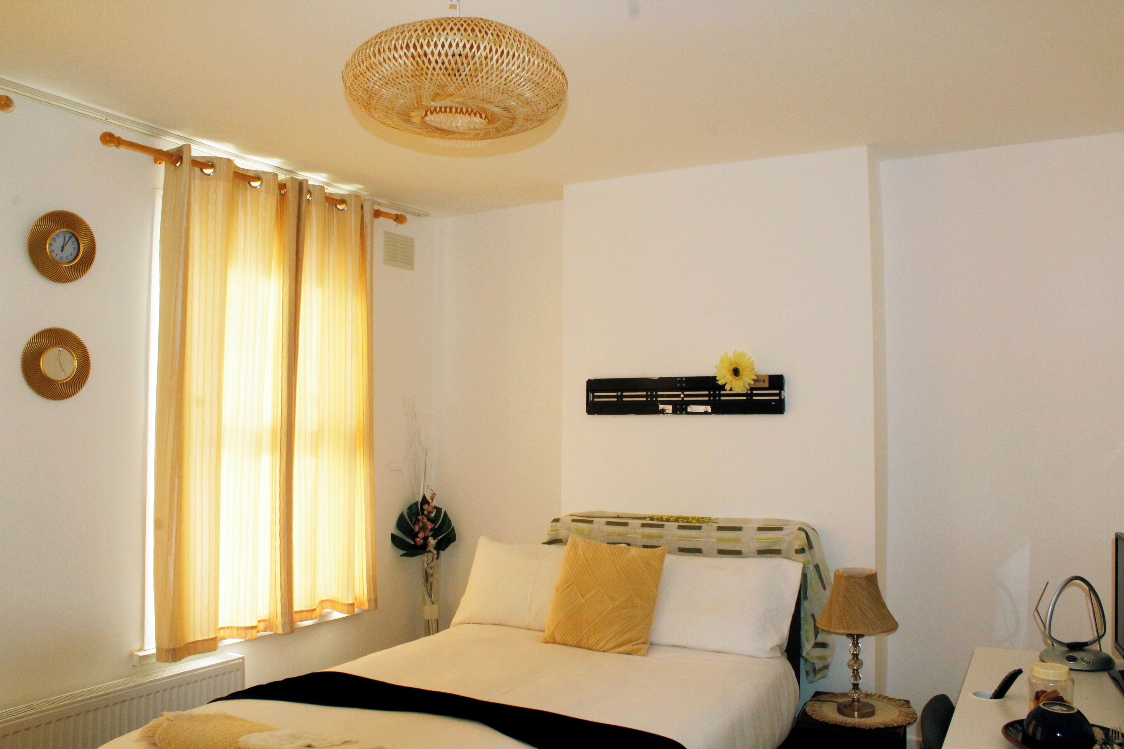 A hotel room with a bed, a desk, a lamp, a computer, and a window with curtains.