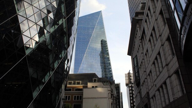 Un grattacielo moderno con facciata in vetro e forma triangolare, circondato da altri edifici dall'architettura tradizionale.