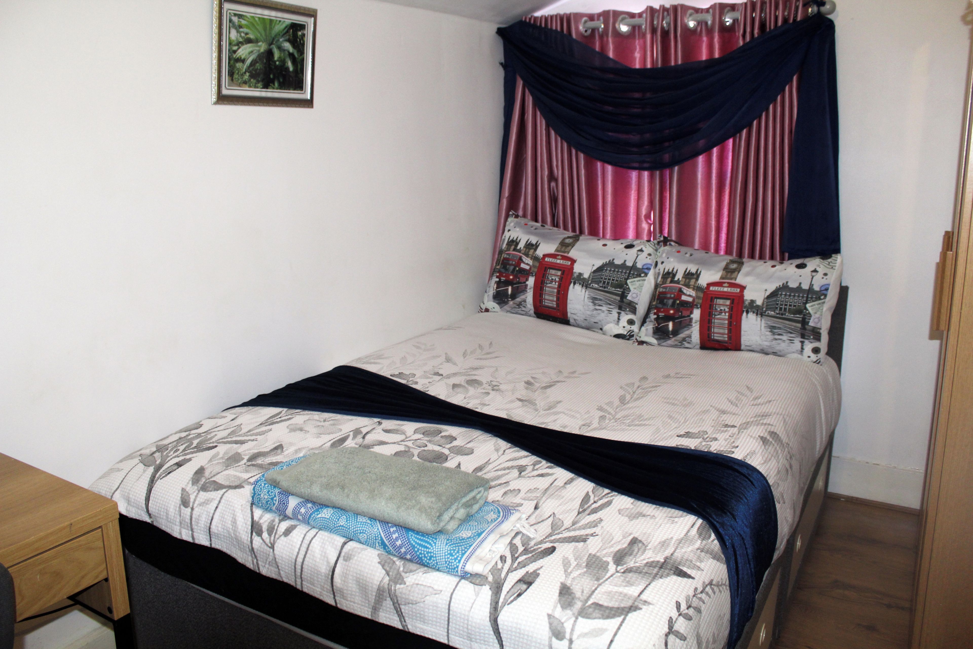 A bed with floral bedding, a dark blue throw, and a pillow with a cityscape design.