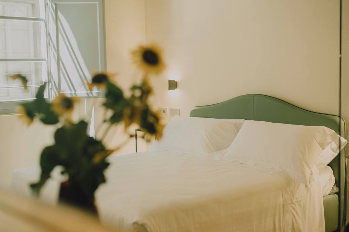 A bed with white linens, a green headboard, and a bedside lamp.