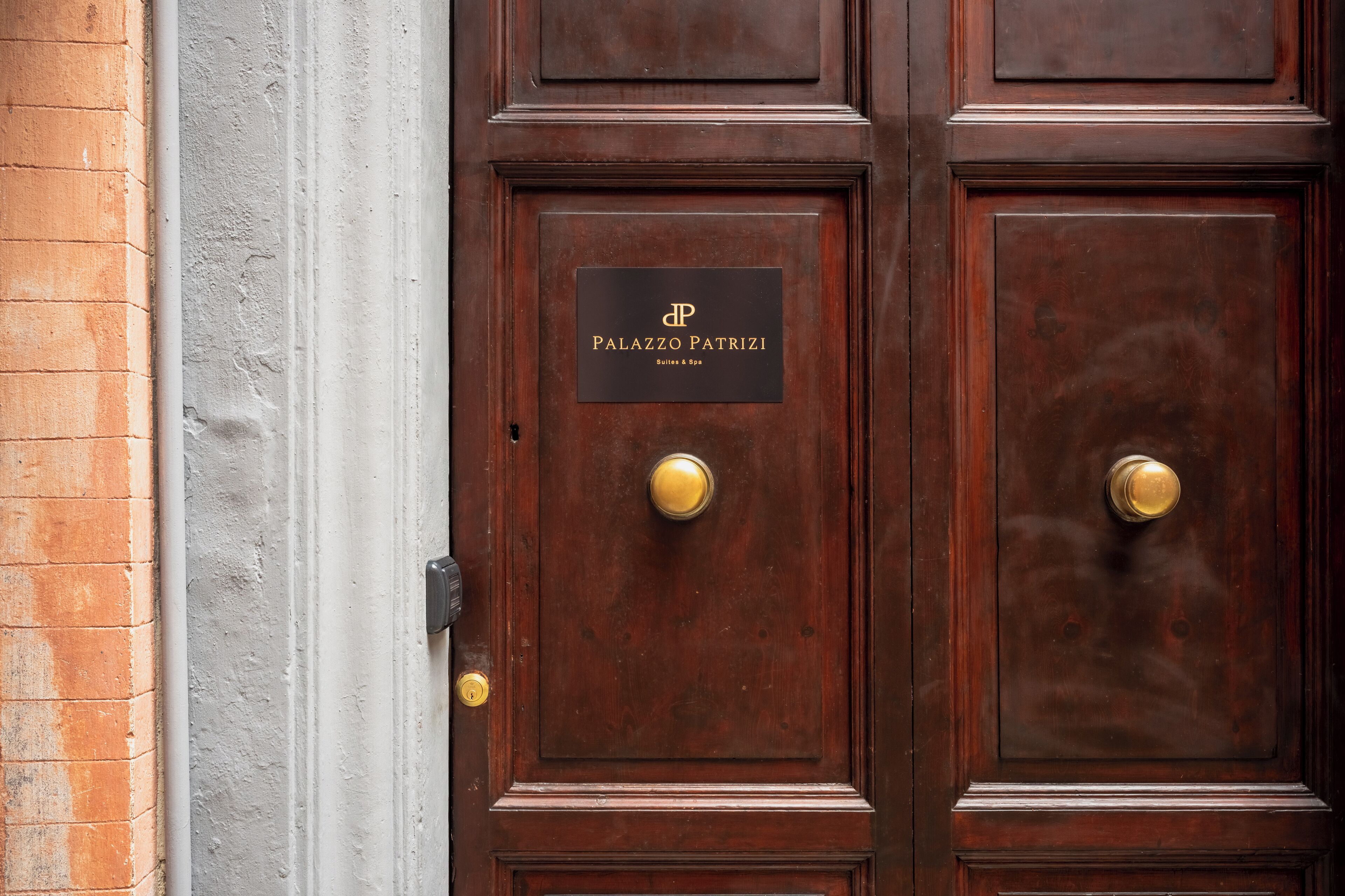 A dark wooden door with a brass doorknob and a plaque reading "Palazzo Patrizi Suites & Spa".