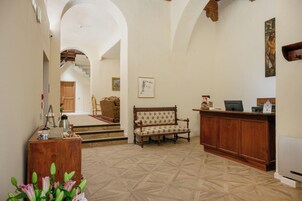 Un'ampia hall con una reception in legno, una panca decorata e una scala che conduce in un'altra zona.
