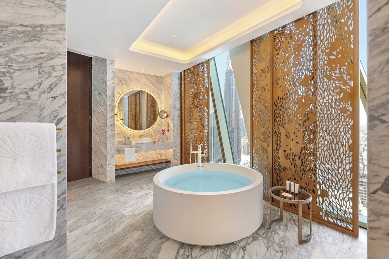 A modern bathroom with a marble floor, a round bathtub, a large mirror, and a decorative partition.