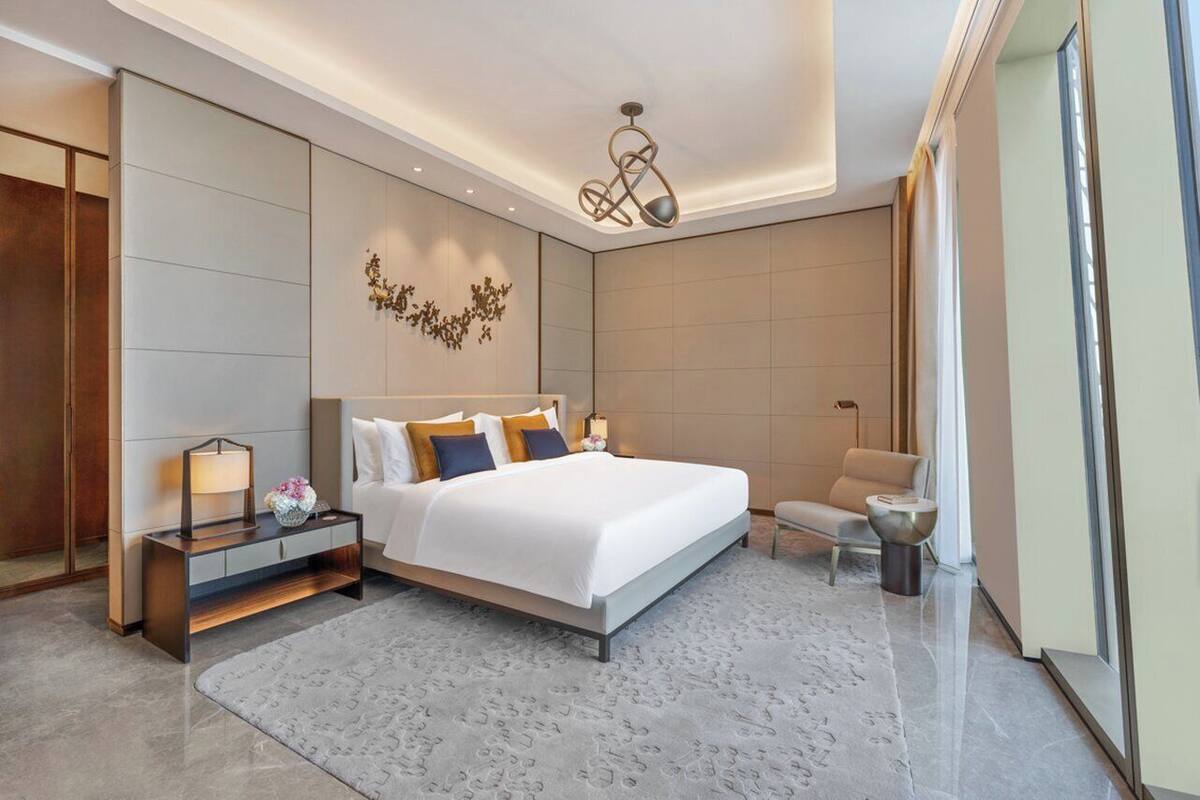 Une chambre d’hôtel moderne avec un grand lit, une table de chevet avec une lampe, une petite table d’appoint et une chaise.