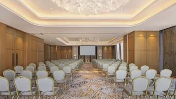 A conference room with rows of chairs, a large screen, and a chandelier.