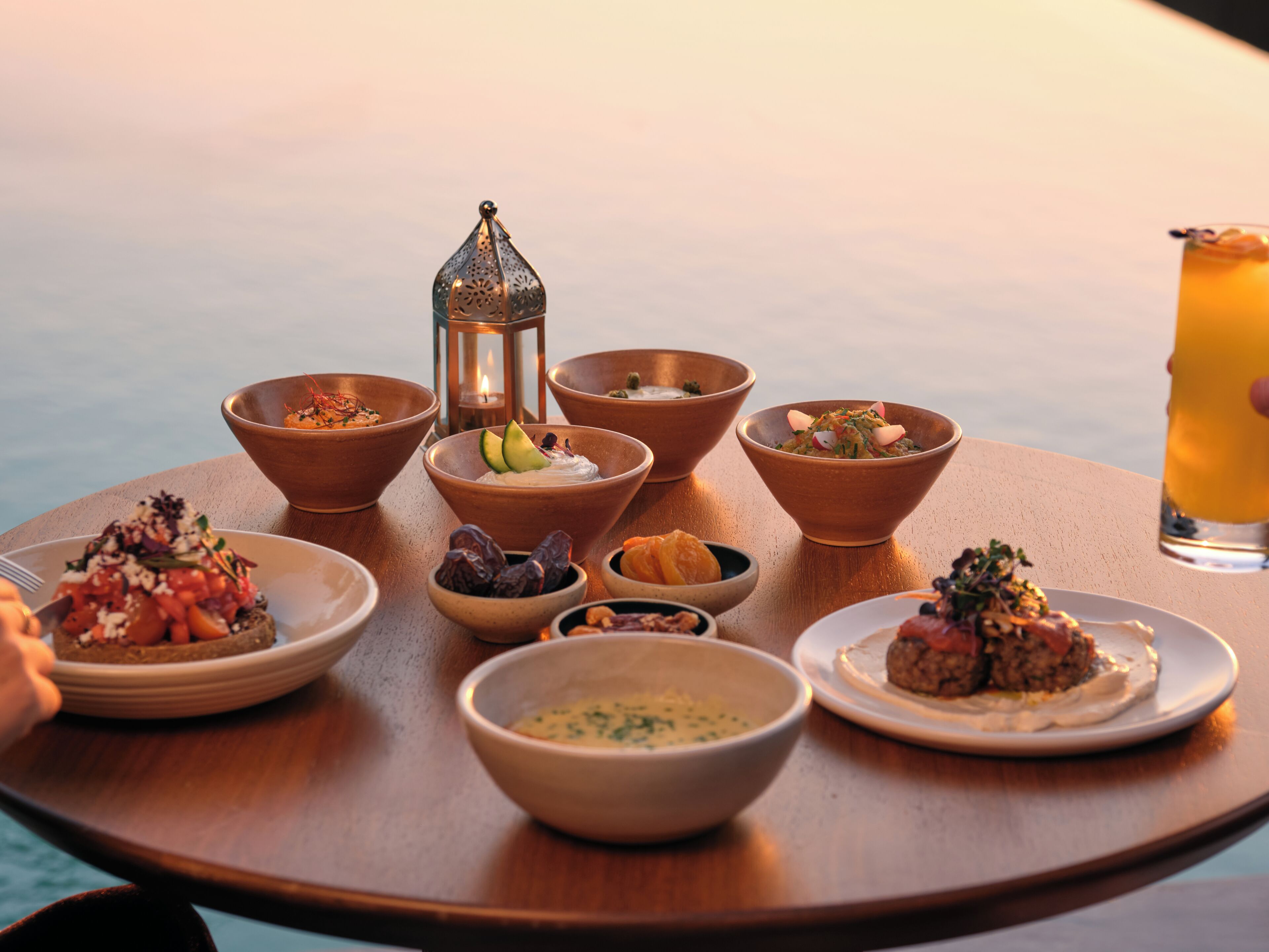 A table with various dishes and a drink, set against a view of the sea.