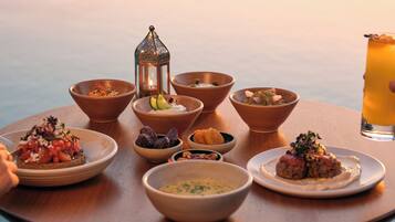 A table with various dishes and a drink, set against a view of the sea.
