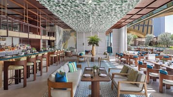 Un grand espace bar doté de hauts tabourets et d’un long comptoir, entouré de sièges confortables et agrémenté d’une grande plante décorative.