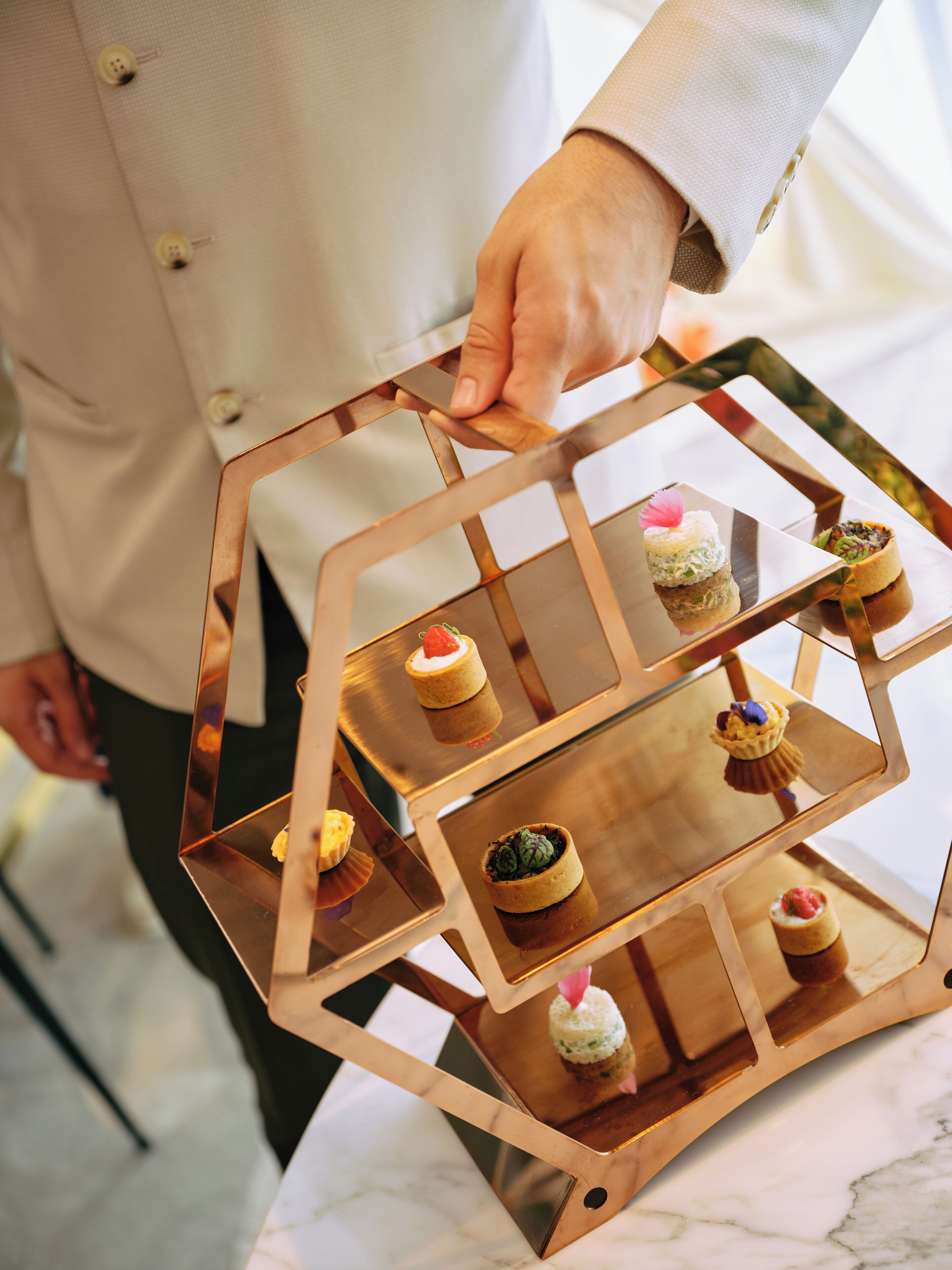 A person holding a hexagonal tray with multiple tiers, each holding a dessert.