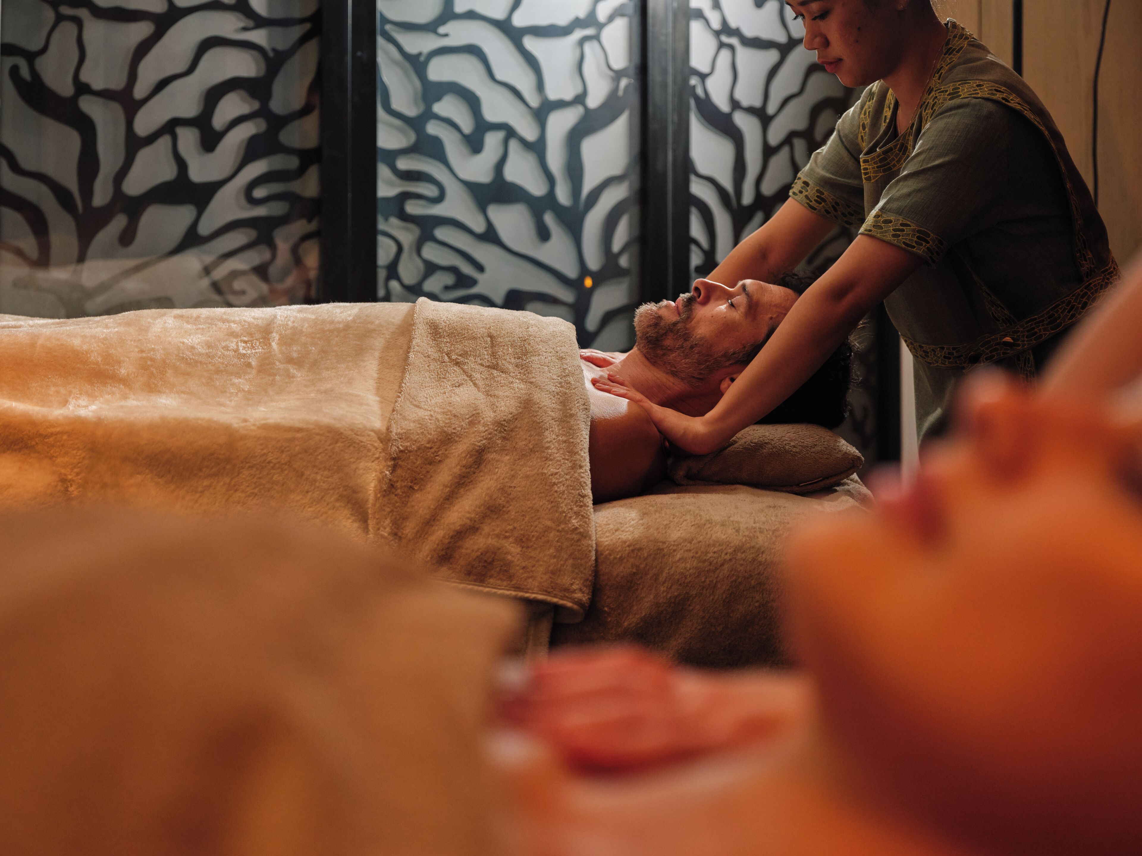 A massage therapy session in a room with patterned walls and a bed with a beige blanket.